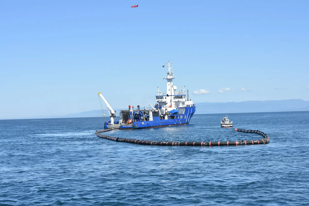 An oil-recovery vessel deploying a containment boom at sea during a drill